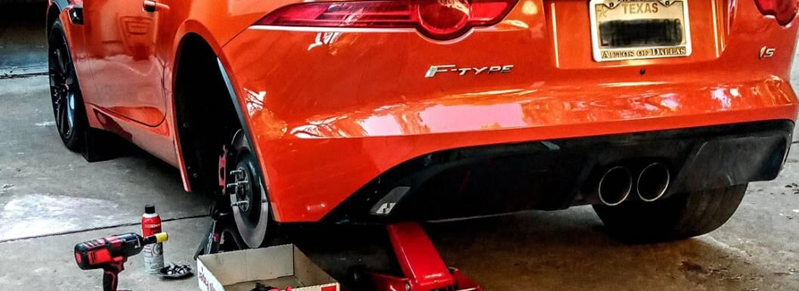 Orange Jaguar F-Type on jack stands for brake service